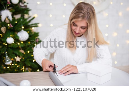 beautiful blond woman packing gifts in living room with decorated Christmas tree
