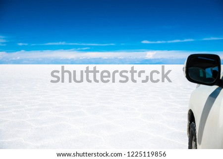 Amazing sunshine scenery of bright white Salar de Uyuni in Bolivia with blue sky and white car side view
