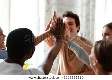 Diverse multiracial cheerful students giving high five greeting each other. Multi-ethnic millennial group of young people slapping palms sitting indoors. Gesture of celebration, friendship and unity Royalty-Free Stock Photo #1225131190