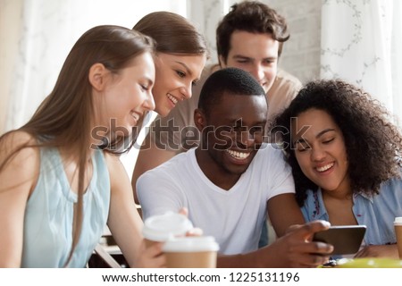 Black guy holding mobile phone watching funny videos with mixed race friends having fun together. Laughing students taking selfie photo looking at cellular screen. Friendship, technology usage concept