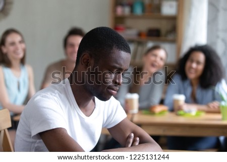 Group diverse people sitting in cafe laughing scoffing at black guy. Focus on sitting separately man feels upset and unhappy, schoolmates not take him to their company. Racial discrimination concept Royalty-Free Stock Photo #1225131244