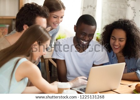 Black african guy with diverse friends watching comedy movie funny videos online using computer sitting together at desk. Friendship between multiracial people and leisure free time activities concept