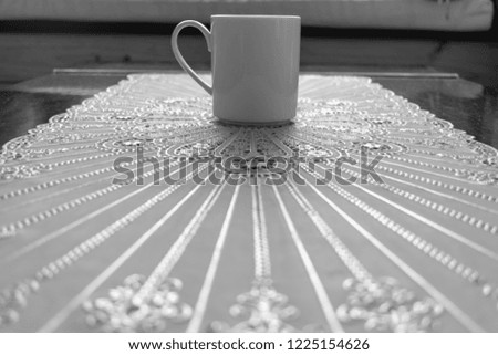 Low angle image of a white coffee mug placed on a white lace pattern table