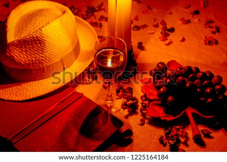 Close-up, beautiful composition in the dark room with candles, old book, hat, grape and glass of vine