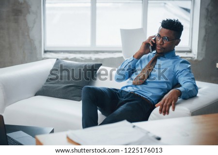 Photo of afro american young guy sitting on a couch and have conversation at phone.