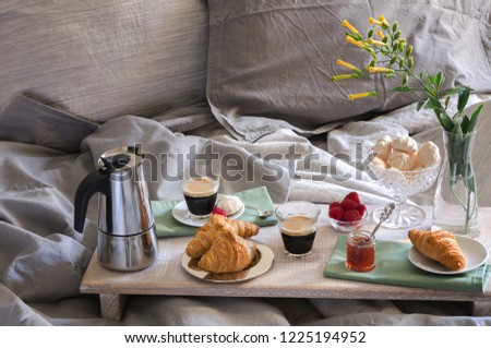 Romantic Breakfast  for two in bed. Coffee maker  and coffee glasses, croissants, jam, raspberry meringue and flowers on wood tray. Romantic good morning scenery