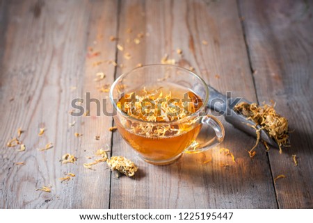 Herbal tea in a transparent glass mug with calendula flowers on a wooden background. Phytotea. Selective focus