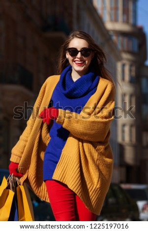 Shopping, sale, black friday concept: young beautiful happy smiling woman wearing stylish colorful kinitted clothes holding paper bags, walking in street of european city