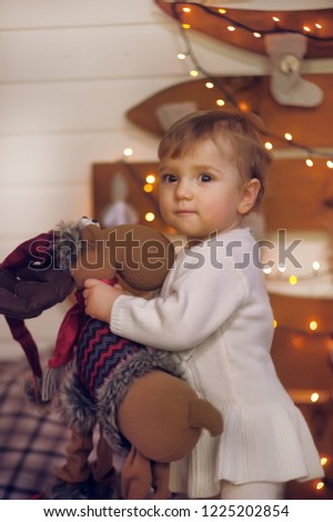 little girl one year old in jeans in christmas with a toy deer