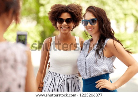 female friendship, technology and people - woman with smartphone photographing her friends in summer park