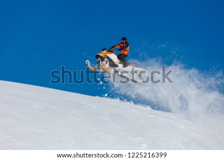 the guy is flying and jumping on a snowmobile on a background of blue sky leaving a trail of splashes of white snow. bright snowmobile and suit without brands. extra high quality  Royalty-Free Stock Photo #1225216399