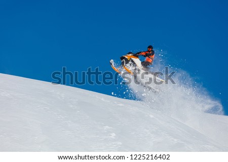 the guy is flying and jumping on a snowmobile on a background of blue sky leaving a trail of splashes of white snow. bright snowmobile and suit without brands. extra high quality  Royalty-Free Stock Photo #1225216402