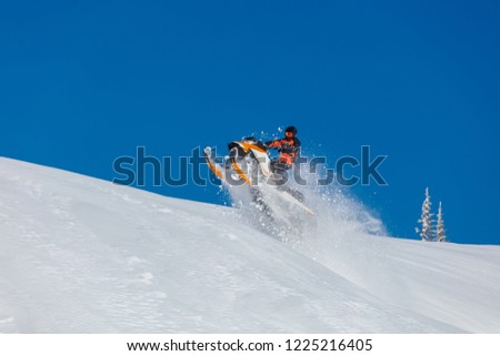 the guy is flying and jumping on a snowmobile on a background of blue sky leaving a trail of splashes of white snow. bright snowmobile and suit without brands. extra high quality  Royalty-Free Stock Photo #1225216405