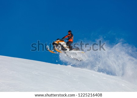 the guy is flying and jumping on a snowmobile on a background of blue sky leaving a trail of splashes of white snow. bright snowmobile and suit without brands. extra high quality  Royalty-Free Stock Photo #1225216408