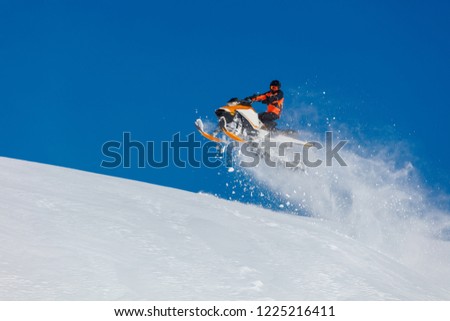 the guy is flying and jumping on a snowmobile on a background of blue sky leaving a trail of splashes of white snow. bright snowmobile and suit without brands. extra high quality  Royalty-Free Stock Photo #1225216411