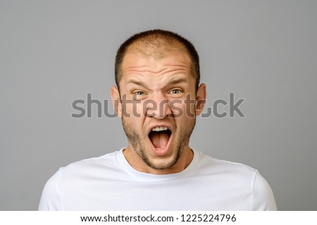 Portrait of angry screaming young man on gray background