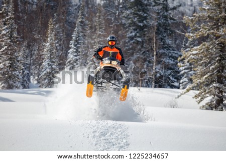 the guy is flying and jumping on a snowmobile on a background of winter forest  leaving a trail of splashes of white snow. bright snowmobile and suit without brands. extra high quality Royalty-Free Stock Photo #1225234657