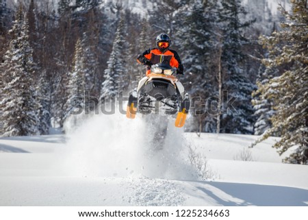 the guy is flying and jumping on a snowmobile on a background of winter forest  leaving a trail of splashes of white snow. bright snowmobile and suit without brands. extra high quality Royalty-Free Stock Photo #1225234663