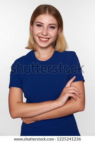 Cheerful young pretty woman in blue dress with her hands folded. Isolated on gray studio background