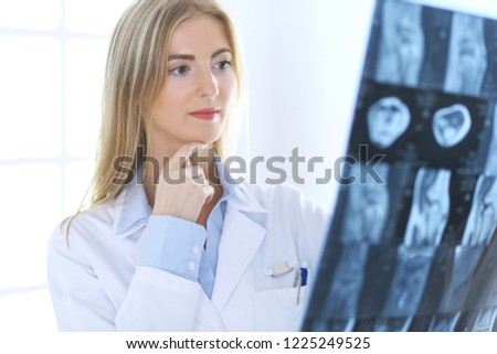 Doctor woman osteopathist examining x-ray picture while standing near window in clinic or hospital. Medicine and healthcare concept