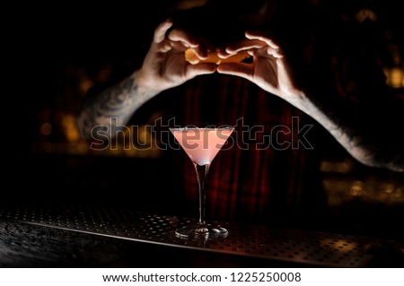 Barman sprinkling fresh orange peel juice into a tasty Cosmopolitan cocktail on the bar counter in dark background
