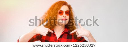 Portrait of beautiful redhead happy young woman in sunglasses smiling showing on blank area on gray background