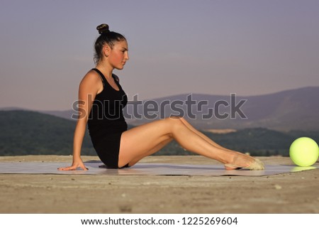 Sport and success. Woman gymnast in black sportswear with green ball. Gymnastic school and energy. Workout of girl on blue sky background. Flexibility in acrobatics and fitness health.