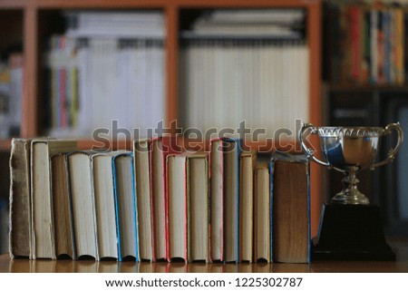 Close-up of old books lying in a row on table in library. Trophies placed near Bookshelf is the background selective focus and shallow depth of field