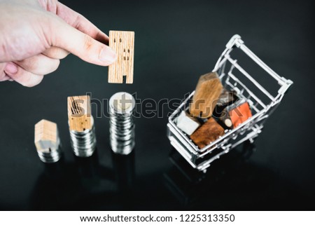 Hand choosing mini wood house from row of coin money with cart on dark table, selective focus, Planning to buy property. Choose what's the best. A symbol for construction ,ecology, loan concepts