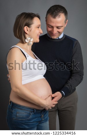 Romantic Couple of handsome husband and pretty pragnant woman posing at studio embracing stomach - Studio Portrait
