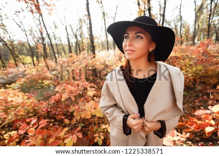 portrait of beautiful woman in black hat and coat on a background of yellow autumn leaves. wide angle