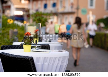 Cafe tables on the street. In the background is a street with human silhouettes.