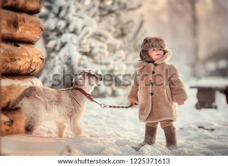 Baby in a fur hat and a fur coat  with a goat. 