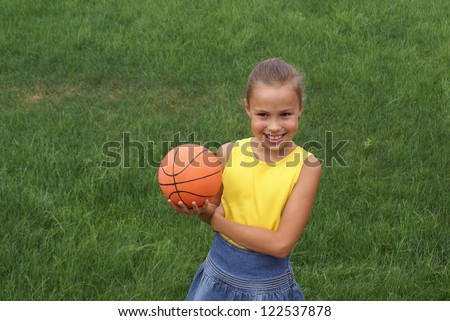 Preteen school girl with basketball on green grass background outdoors