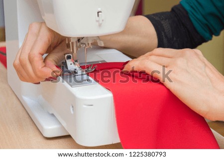 Woman's hands working with sewing machine. Making new, modern, classic dress, blouse, trousers or other clothes. Red fabric. Handmade work. Feminine hobby. Closeup.