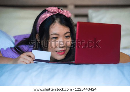 young beautiful and happy Asian Chinese woman using credit card internet banking on laptop computer at home in bed smiling cheerful shopping online buying in e-commerce and lifestyle concept