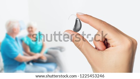 Doctor showing a last generation of hearing aid device with unfocused senior patients in background Royalty-Free Stock Photo #1225453246
