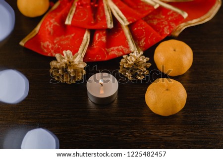 Christmas or Christmas composition with a candle, a mandarins, a New Year red bow, golden fir cones , on a wooden background with a bokeh effect