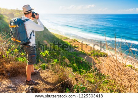 Traveling photographer with camera stands on top mountain cliff on background scenic nature landscape tropical island