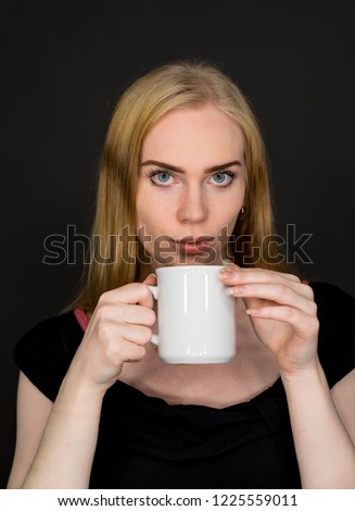 Young woman drinking coffee. Blonde girl with white tea cup on a gray background