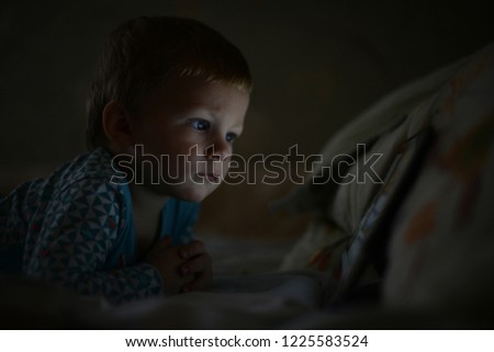 child boy watching a cartoon on a tablet, baby plays games on a tablet, learns multimedia. Addiction