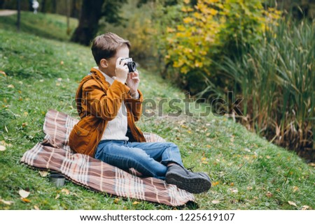 Cute boy walks and poses in a colorful autumn Park.  The boy takes pictures on the camera. Toning.