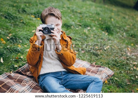 Cute boy walks and poses in a colorful autumn Park.  The boy takes pictures on the camera. Toning.
