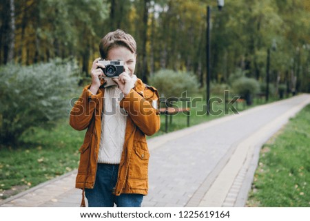 Cute boy walks and poses in a colorful autumn Park. The boy takes pictures on the camera. Toning.