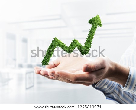 Palms of businessman in suit presenting green plant in form of growing graph. Mixed media