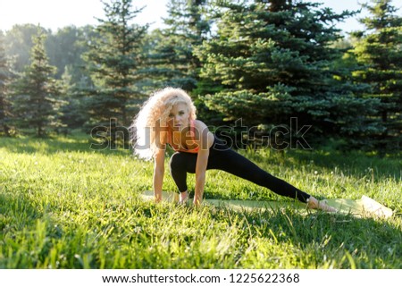 Image of young curly-haired sports woman practicing yoga on rug in park