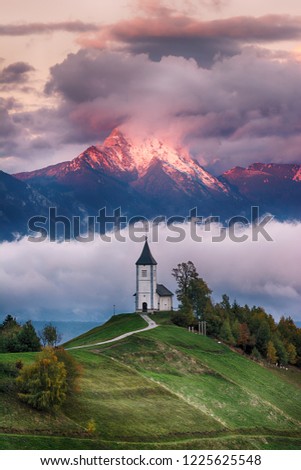 Beautiful sunrise landscape of church Jamnik in Slovenia on green hill with blue cloudy sky and mountains background
