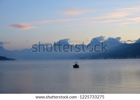 Long exposure picture of scenic view of Lake McDonald with a recreational boat during sunrise by the going-to-the-sun road,  looking at the mountains with a beautiful sky, at Glacier National Park