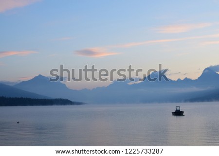 Long exposure picture of scenic view of Lake McDonald with a recreational boat during sunrise by the going-to-the-sun road,  looking at the mountains with a beautiful sky, at Glacier National Park