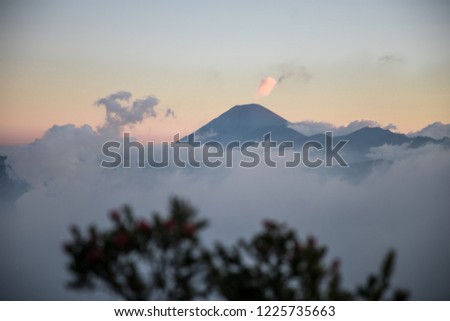 Clouds cover Mount Bromo during sunset with a small view of Mount Semeru in the distance in East Java, Indonesia
